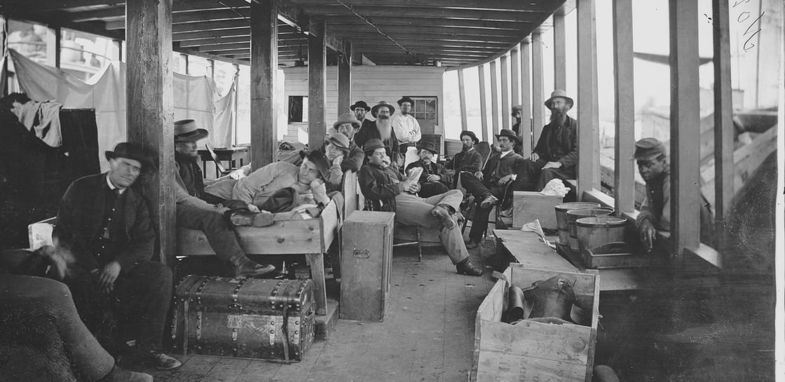 Black and white photograph of a group of men sitting between decks on a steamer ship.