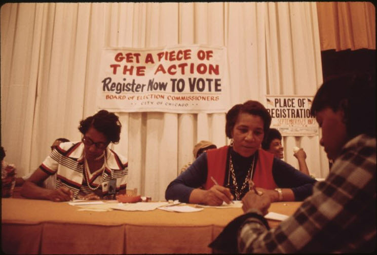 Color photograph of two women working at a table at a voter registration drive. 