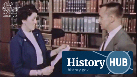 Animated GIF of an archivist and a researcher looking at a document together. Shelves of books and binders are behind them.