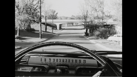 Black and white animated GIF of a car driving down the road from the perspective of being behind the steering wheel