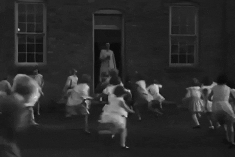 Black and white animated gif of schoolchildren lining up at the door of school while the schoolteacher rings a bell.