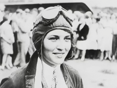 Animated GIF of Ruth Elder, wearing a flying helmet and googles, smiling and laughing while talking.