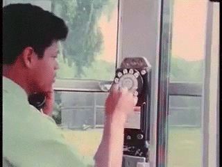 Animated GIF of a boy dialing a rotary phone mounted to the wall. The GIF zooms in on the phone